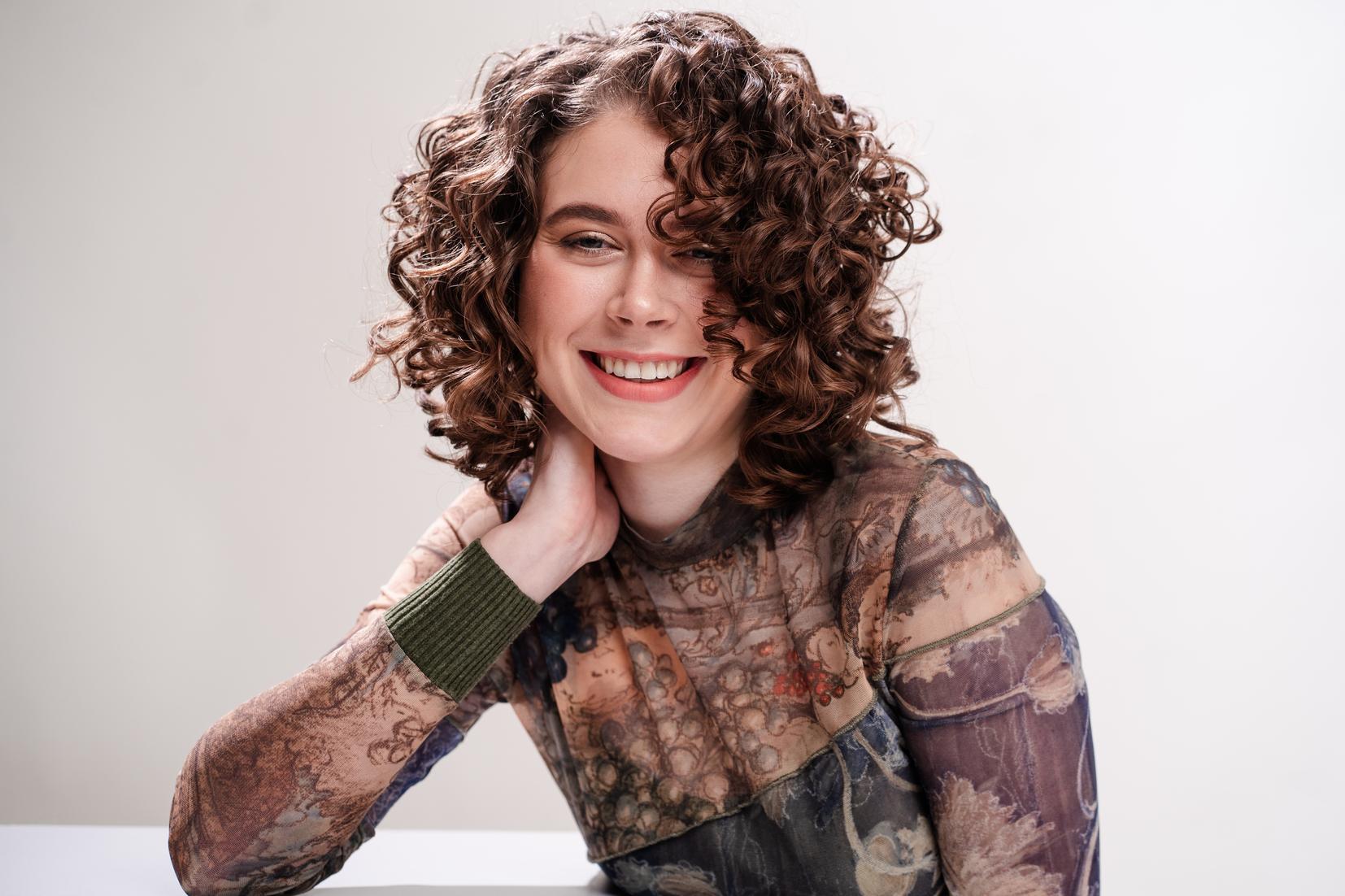 Frau mit kurzen, braunen Locken l&auml;chelt entspannt in die Kamera