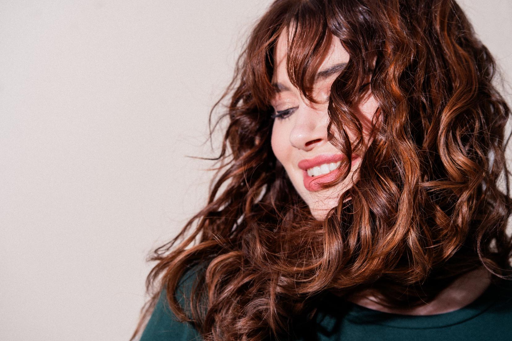 Portr&auml;t einer Frau mit langen, braunen Locken und sanfter Bewegung im Haar